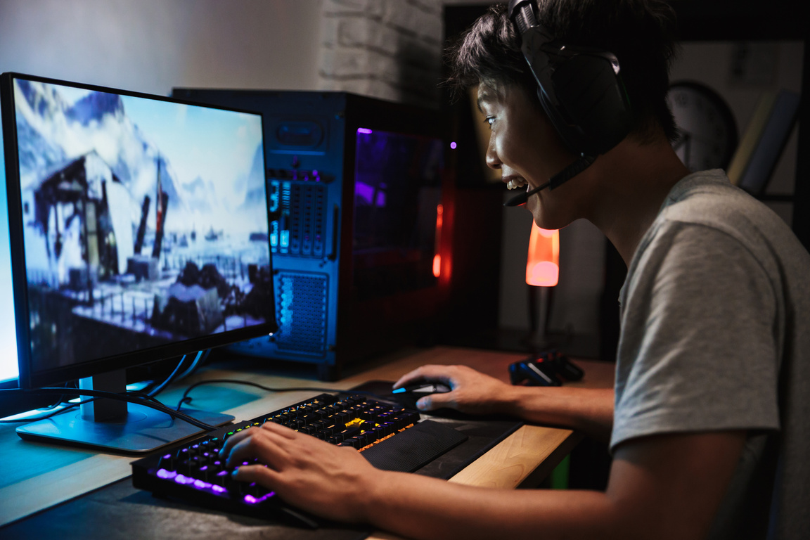 Asian Cheerful Gamer Boy Playing Video Games Online on Computer